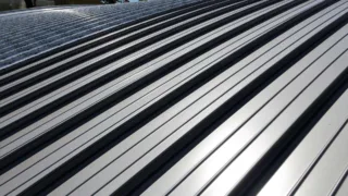Close-up view of a silver metal roof with clean, evenly spaced ridges and panels reflecting sunlight.
