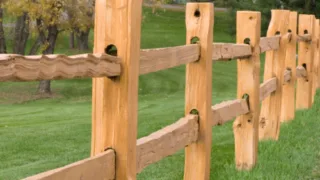Wooden fence installed on a grassy landscape with trees in the background.