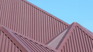 Red metal sheet roofing with multiple sloped sections under a clear blue sky