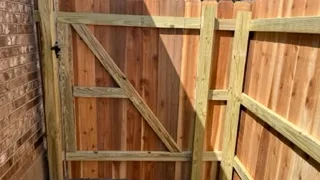 Wooden fence gate with diagonal support brace between two brick houses.