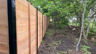 Newly installed wooden privacy fence running along a tree-lined yard.