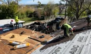 Workers installing roofing materials on a house under renovation with tools and supplies on the roof.