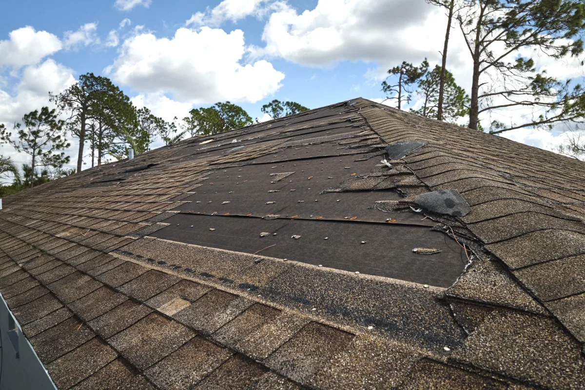 Damaged house roof with missing shingles after hurricane Ian.